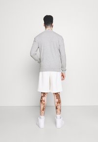 Szary sweatshirt z długimi rękawami, ribbami przy mankietach i u dołu. Połączony z białymi szortami, podkreślającymi teksturowaną skórę i białe sneakersy.