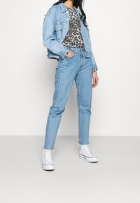 Helles blaugraues Jeansjackett, graues Leopardenmuster-T-Shirt, hochgeschnittene hellblaue Jeans und weiße hohe Sneaker mit ausgefranstem Saum.