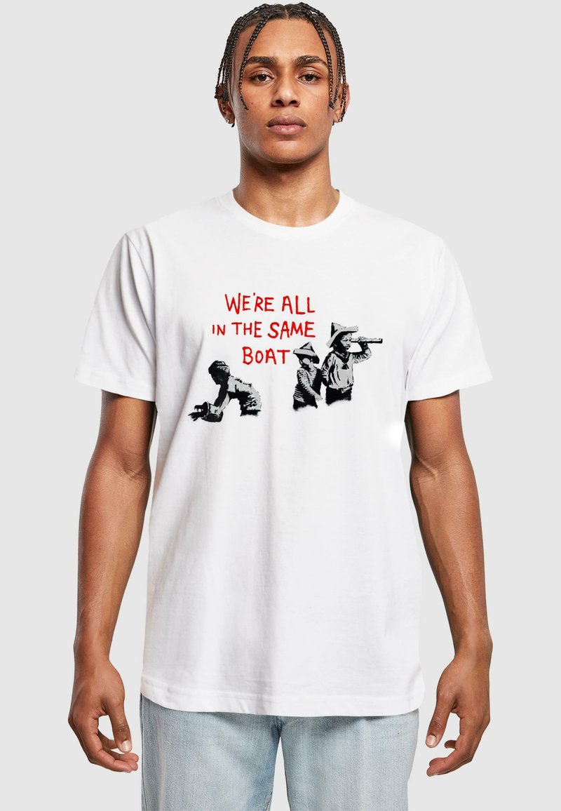 Hvid bomulds T-shirt med teksten "VI ER ALLE I DEN SAMME BÅD" i rød, ledsaget af sorte grafiske illustrationer af figurer.