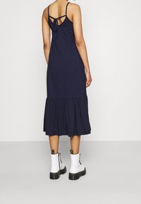 Marinblå klänning med utsvängd nederkant, ryggslut med knytdetalj och justerbara axelremmar. Kombinerad med vita ankelstövlar med svarta sulor.