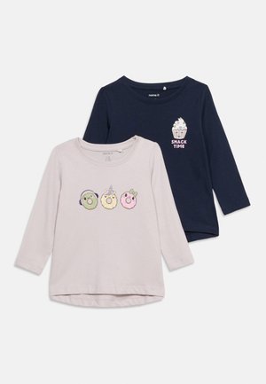 Deux chemises à manches longues pour enfants, une bleu marine avec un cupcake et l'inscription "Snack Time", une rose pâle avec trois beignets décorés portant des écouteurs, une corne de licorne et un nœud.