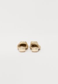 Sandales glissantes dorées avec une texture tissée et un talon bas. Dotées d'une sangle à boucle sur le dessus pour un maintien sécurisé. Doublure intérieure lisse.