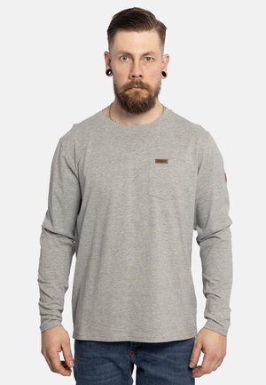 Hellgraues langärmliges T-Shirt mit Rundhalsausschnitt, ausgestattet mit einer linken Brusttasche und einem kleinen braunen Etikett. Getragen mit blauen Jeans.