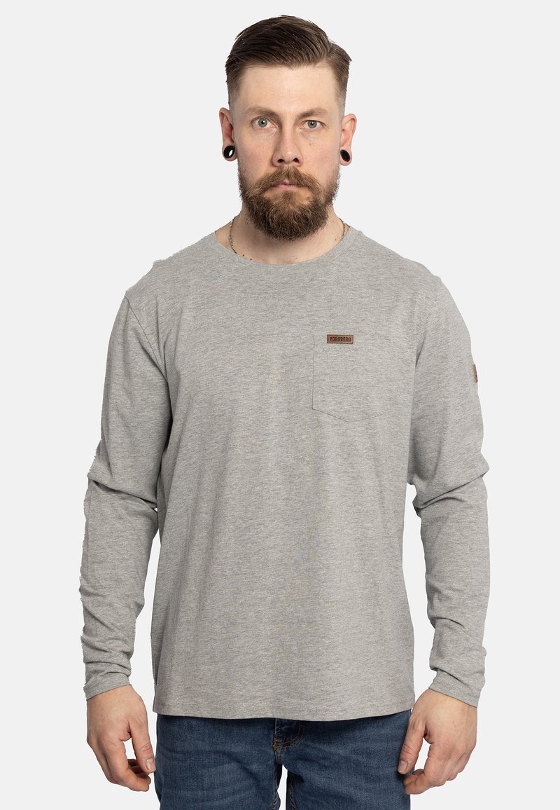 Hellgraues langärmliges T-Shirt mit Rundhalsausschnitt, ausgestattet mit einer linken Brusttasche und einem kleinen braunen Etikett. Getragen mit blauen Jeans.