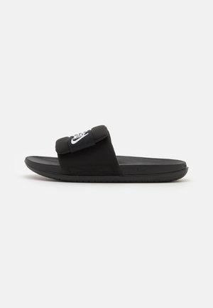 Schwarze Flip-Flops mit flacher Sohle, aus synthetischem Material. Sie verfügen über einen breiten Riemen mit einem auffälligen weißen Nike-Logo. Glatte Textur.