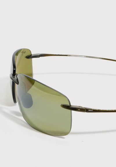 Γυαλιά ηλίου χωρίς σκελετό με φακούς πράσινου χρώματος και λεπτούς, σκουρόχρωμους μεταλλικούς βραχίονες σε λευκό φόντο.