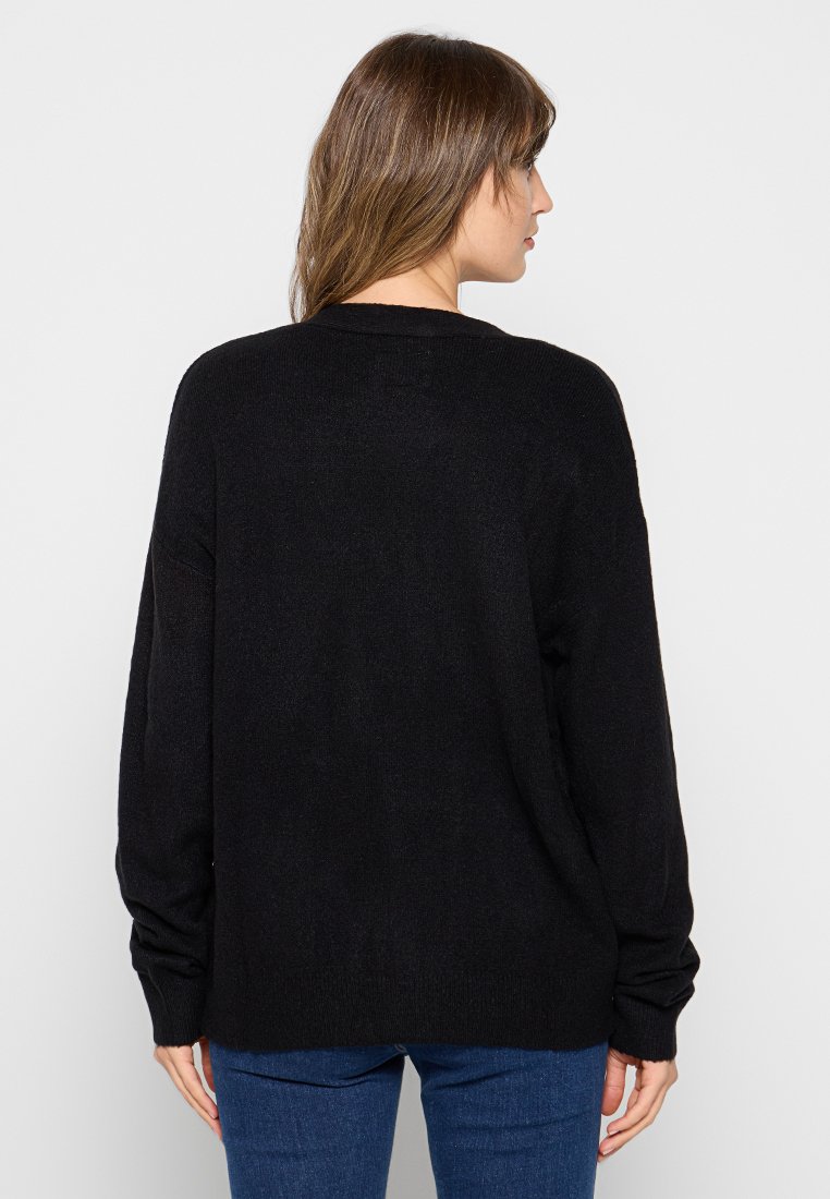 Suéter negro de punto oversized con mangas largas, cuello redondo y una textura sutil. Diseño simple sin patrones ni adornos.