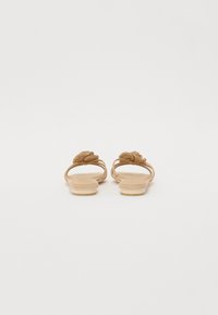 Tan flat sandals with woven accents on the straps, a smooth sole, and a minimalistic design. The background is plain white.