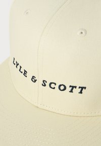 Gorra de béisbol de tela beige con el logotipo bordado en negro "Lyle & Scott" en el panel frontal y ojales de ventilación cosidos.