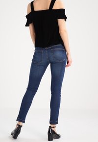 Svart off-shoulder-topp med volangkant på ärmarna, kombinerad med blå skinny jeans med blekt tvätt och ankellång längd. Svarta klackskor.