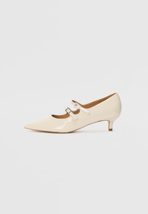 Chaussures Mary Jane en cuir verni beige avec deux boucles ajustables, bout pointu et un petit talon. Texture lisse avec un fini brillant.