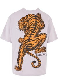 Hvit oversized t-skjorte med et svart og oransje grafikk av en tiger i en dynamisk posisjon, med sterke striper og en detaljert design.