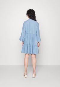 Ljusblå chambrayklänning med trekvartsärmar, volangärmar och en lagd kjoldesign. Slät teknik med en avslappnad passform.