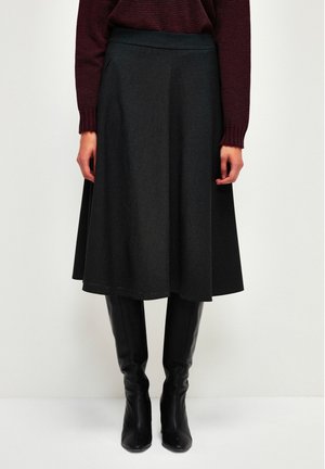 Une jupe évasée grise en mélange de laine douce, dotée d'une taille lisse et atteignant le mollet, associée à des bottes noires ajustées arrivant aux genoux.
