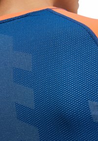 Niebieska sportowa koszulka z teksturowanej tkaniny, z pomarańczowym akcentem przy kołnierzy; wzór z delikatnym logo na plecach.