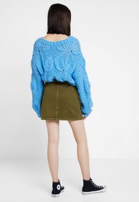 Maglione blu oversize lavorato a maglia con motivi a foglia, abbinato a una mini gonna verde oliva e sneakers alte nere. Vista posteriore.