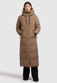 Abrigo largo acolchado marrón con capucha, con grandes secciones acolchadas horizontales, cremallera frontal y bolsillos laterales. Detalles en negro realzan el diseño.