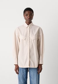 Camicia button-up a righe beige e bianche con due tasche sul petto, maniche lunghe e colletto standard. Vestibilità leggermente rilassata, texture liscia.