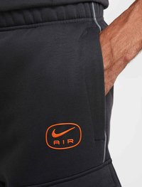 Svarta sportshorts i mjukt tyg med en orange Nike "AIR"-logotyp på fickan och gråa accentstygn.