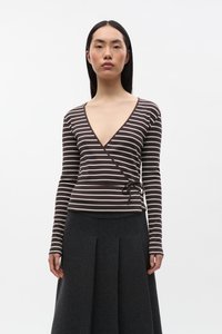 Bruin en crèmekleurig gestreept wikkelshirt met lange mouwen en een diepe V-hals, voorzien van een strikdetail in de taille. Gecombineerd met een donkere geplooide rok.
