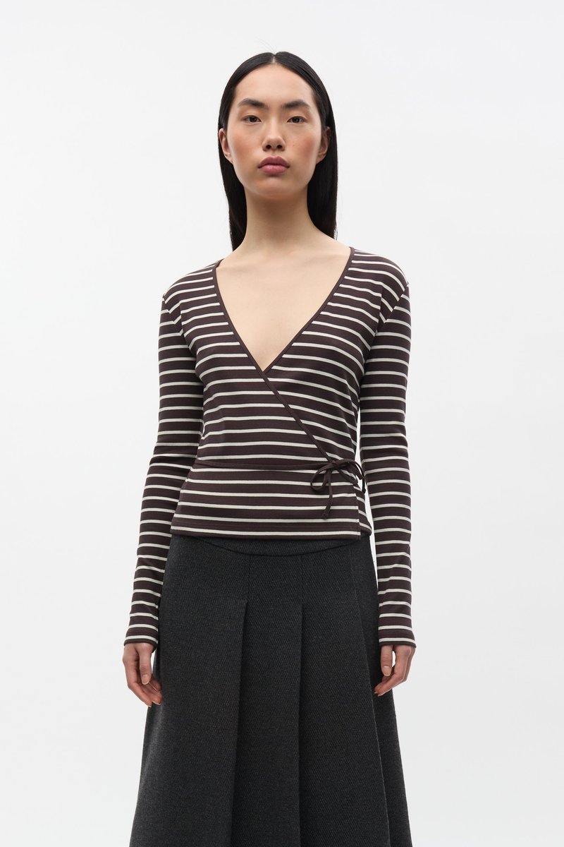 Bruin en crèmekleurig gestreept wikkelshirt met lange mouwen en een diepe V-hals, voorzien van een strikdetail in de taille. Gecombineerd met een donkere geplooide rok.