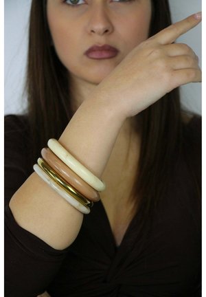 Set van vier armbanden om een arm: creme-, tan- en goudkleurig. Soepele en glanzende materialen, met een gelaagd ontwerp en verschillende breedtes.