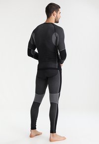 Set di abbigliamento sportivo nero per uomini, composto da una maglia aderente con motivi testurizzati e leggings coordinati con dettagli a griglia e cuciture bianche.