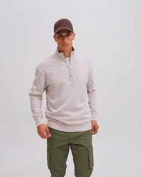 Beige zippered sweatshirt with elastic cuffs, paired with green cargo pants featuring multiple pockets. Brown cap completes the outfit.