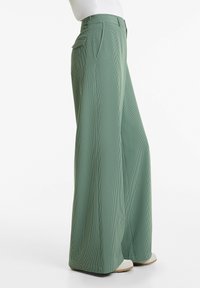 Pantalons larges verts en tissu texturé avec un motif à carreaux, dotés de plis et de poches latérales, présentés debout.