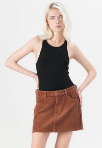 Black ribbed tank top paired with a rust-colored corduroy mini skirt featuring a button closure and front pockets. Smooth texture, fitted design.