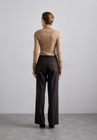 Figurbetontes beiges Rollkragenpullover mit langen Ärmeln, kombiniert mit hochtaillierten dunkelbraunen Hosen, von hinten betrachtet.