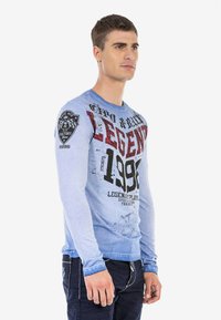 Langarmshirt in Blau mit dem Text "LEGEND" in Schwarz und Rot, mit strukturiertem Finish und Logodetail am linken Ärmel.
