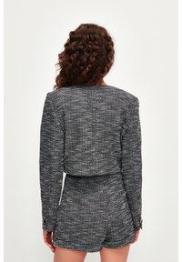 Chaqueta de tweed en blanco y negro con mangas largas y detalle de botones dorados, combinada con pantalones cortos a juego, vista desde la parte posterior.