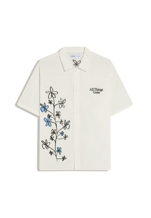 Witte korte mouwen blouse met knopen, zwart en blauw bloemmotief aan de linkerkant en tekst "All Things Gone" op de rechterborst.