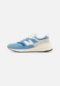 Sneaker azzurro chiaro con texture diverse in suede e mesh, accento di logo bianco, suola imbottita e un dettaglio sul tallone grigio in contrasto.