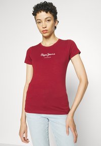 Raudona trumpa rankovė t-shirt, pagaminta iš švelnios medžiagos, turi apvalią iškirptę ir baltą tekstinį logotipą "Pepe Jeans London" priekyje.