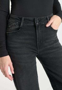 Zwarte denim jeans met een hoge taille, voorzien van een knoopsluiting en zijzakken. De stof heeft een gladde, licht versleten textuur.