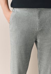 Světlé šedé kalhoty z texturované látky, vybavené bočními kapsami a přímým střihem. Látka má jemný melírovaný vzor.