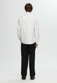 Camicia a righe in tessuto leggero, con una vestibilità rilassata, maniche lunghe e orlo arrotondato. Abbinata a pantaloni neri larghi e scarpe nere.
