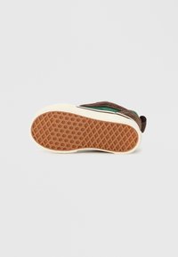 Üks roheline ja pruun tenniseken, mille allosa on näha, rõhutades pruuni vahvli musteriga kummitalda.