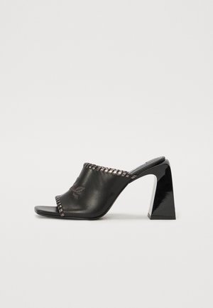 Black leather mules with a wide opening, featuring a stitched trim and a block heel. Smooth texture and minimalist design.
