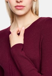 Weinrotes, geripptes Langarmshirt mit V-Ausschnitt, eng anliegendes Design. Weiche Textur mit deutlich sichtbarem Strickmuster.