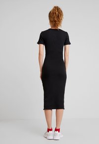 Robe midi noire avec des côtes, à manches courtes, silhouette ajustée et décolleté rond. Associée à des baskets blanches avec des accents rouges.