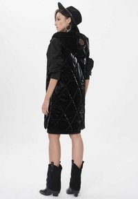 Czarna pikowana kamizelka puchowa z kapturem, z wysokim kołnierzem i bocznymi kieszeniami. Połączona z czarną sukienką i czarnymi botkami do kolan.