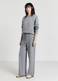 Felpa grigia con maniche lunghe e polsini a coste, abbinata a pantaloni larghi grigi con vita regolabile e cuciture a contrasto.