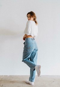 Hellblaue, lässige Jeans mit sichtbaren Stichdetails an der Gesäßtasche, kombiniert mit einem weißen, cropped T-Shirt und weißen Sneakers.