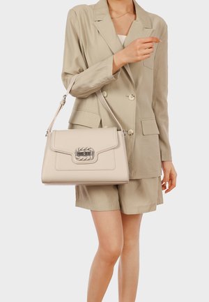 Donna che indossa un blazer beige e pantaloncini, tiene una borsa beige con chiusura argentata per la tracolla.