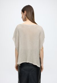 Pulover cu mâneci scurte, lejer, din țesătură tricotată bej deschis, cu decolteu rotund și fante laterale. Asortat cu o fustă neagră din piele.