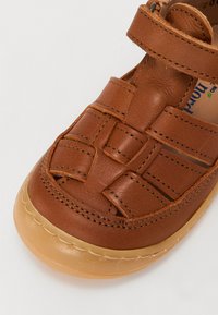 Bruna läder-sandaler med ett vävt mönster, justerbar rem och gummiyttersula. Slät textur med kontrasterande sömnadsdetaljer.