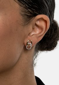 Gold-tone earrings featuring a looping, intertwined design, accented with clear crystals, showcasing a contemporary geometric shape.